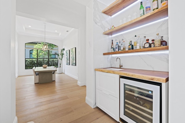 bar with beverage cooler, wood counters, pendant lighting, white cabinets, and light wood-type flooring