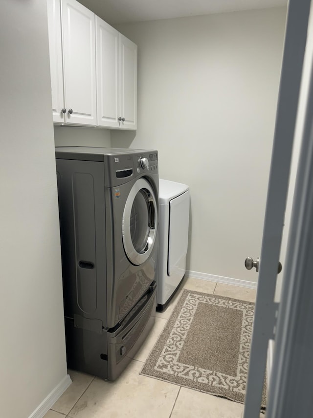 laundry area with washing machine and dryer, light tile patterned floors, and cabinets