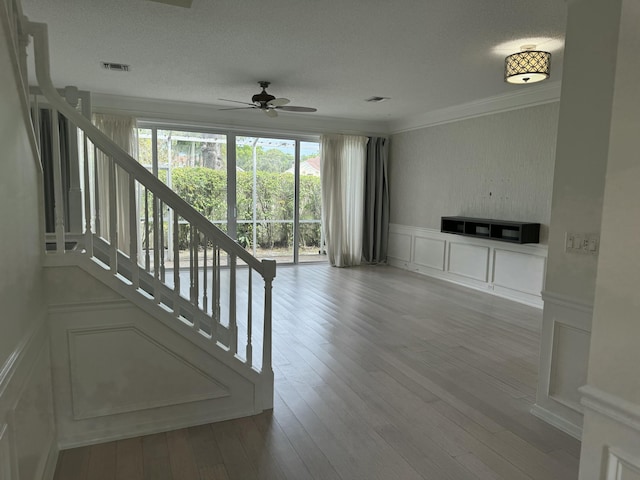 unfurnished living room featuring ceiling fan, a textured ceiling, light hardwood / wood-style flooring, and ornamental molding