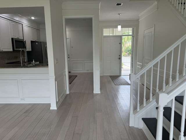 foyer with decorative columns, light hardwood / wood-style floors, sink, and crown molding