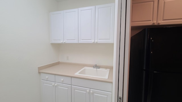 kitchen with freestanding refrigerator, a sink, white cabinetry, and light countertops