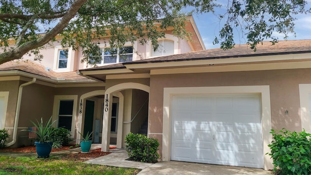 entrance to property featuring a shingled roof, stucco siding, and concrete driveway
