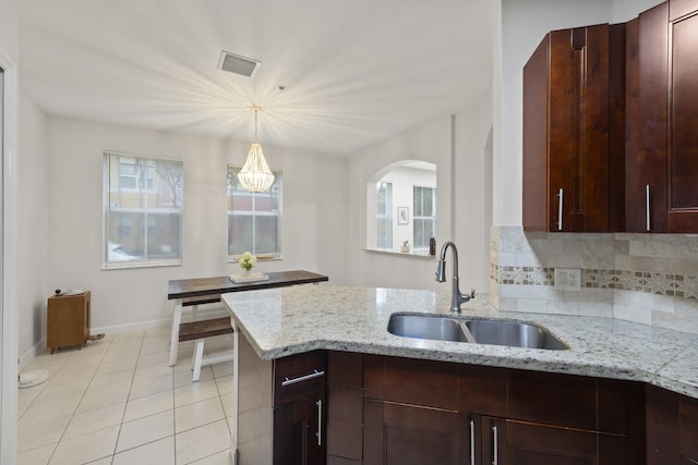 kitchen with pendant lighting, sink, decorative backsplash, light tile patterned floors, and light stone countertops