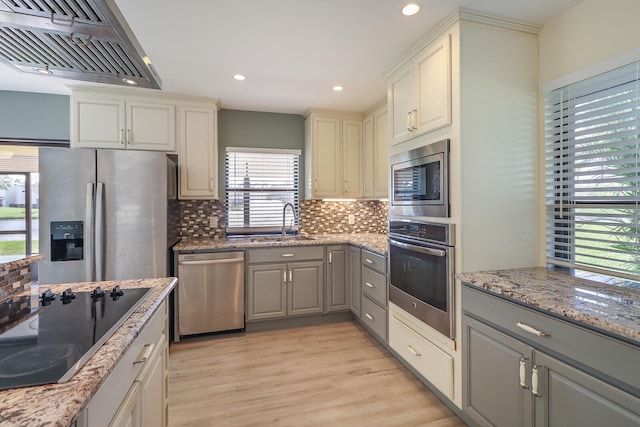 kitchen featuring gray cabinetry, a healthy amount of sunlight, stainless steel appliances, and wall chimney range hood