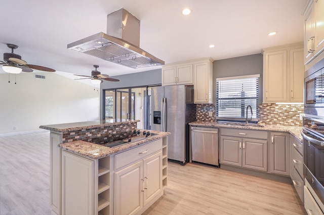 kitchen featuring light stone countertops, sink, light hardwood / wood-style flooring, island exhaust hood, and appliances with stainless steel finishes