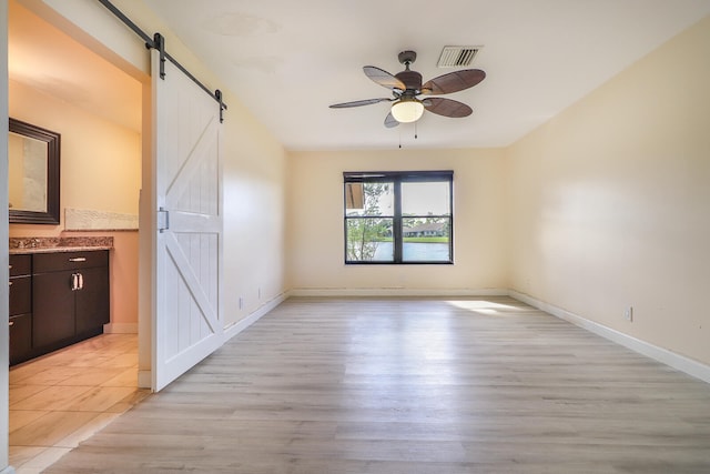 unfurnished room featuring ceiling fan, a barn door, and light hardwood / wood-style floors