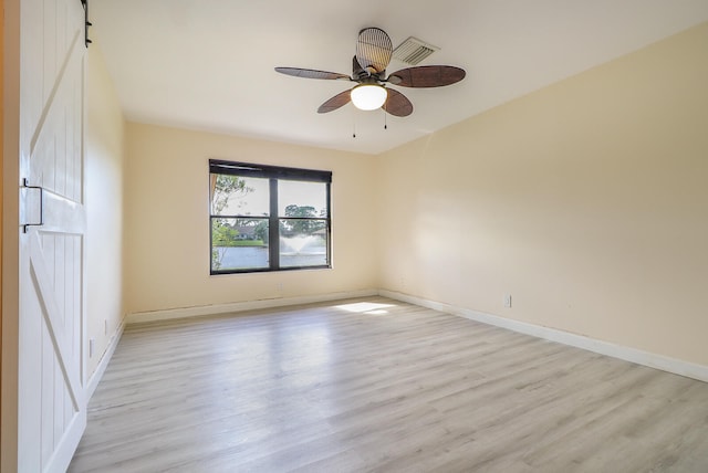 spare room with a barn door, light hardwood / wood-style flooring, and ceiling fan