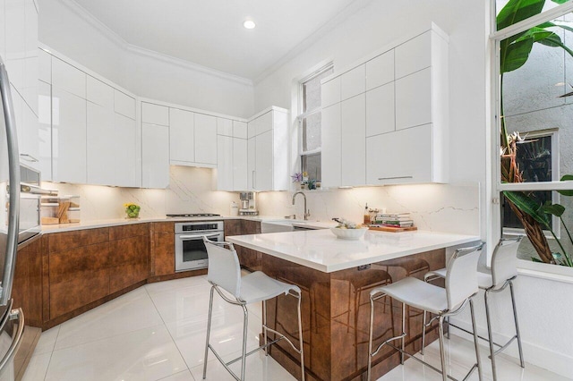 kitchen featuring ornamental molding, a kitchen breakfast bar, appliances with stainless steel finishes, and white cabinetry