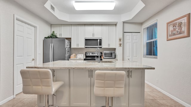 kitchen featuring appliances with stainless steel finishes, a kitchen bar, light stone countertops, and an island with sink