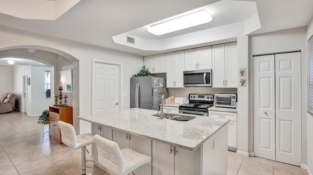 kitchen featuring white cabinets, sink, a center island with sink, appliances with stainless steel finishes, and light stone countertops