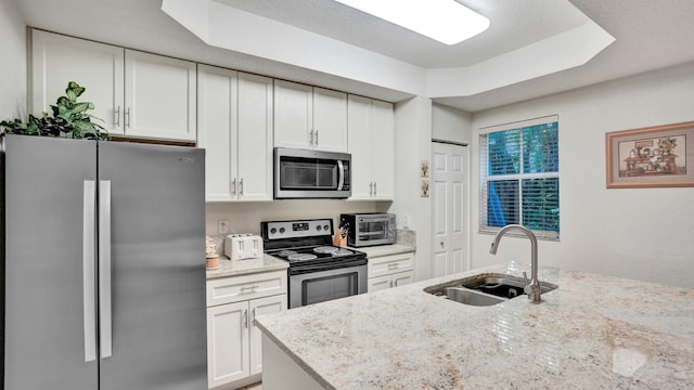 kitchen with a textured ceiling, sink, white cabinetry, stainless steel appliances, and light stone countertops