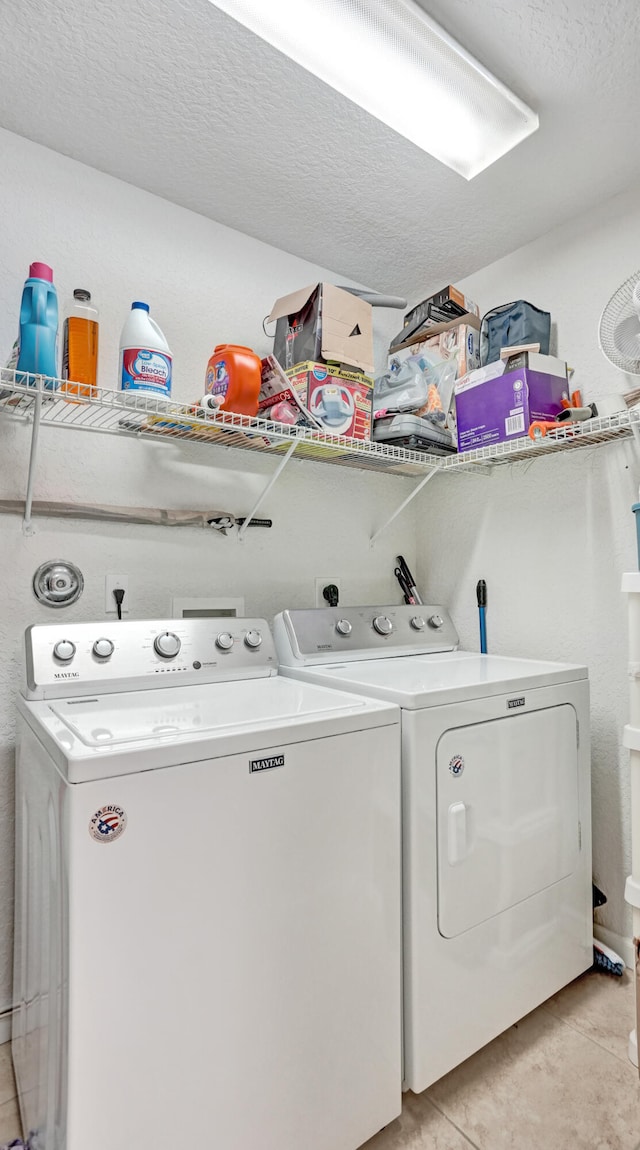 clothes washing area featuring a textured ceiling, light tile patterned floors, and washing machine and clothes dryer