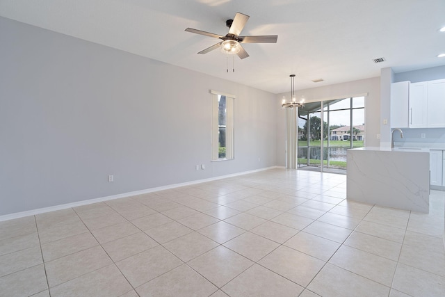 tiled empty room featuring ceiling fan with notable chandelier and sink