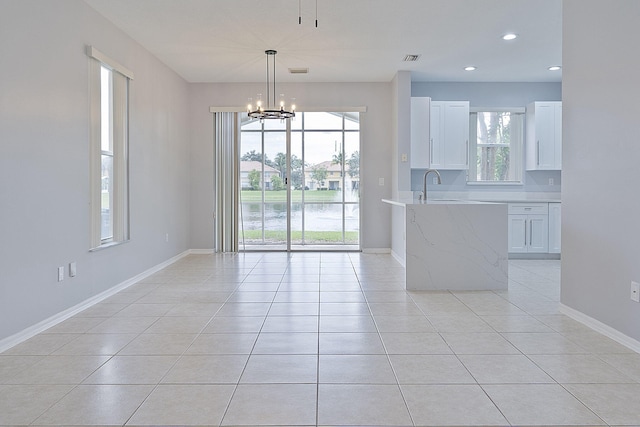 interior space with hanging light fixtures, light tile patterned flooring, light stone countertops, and white cabinets