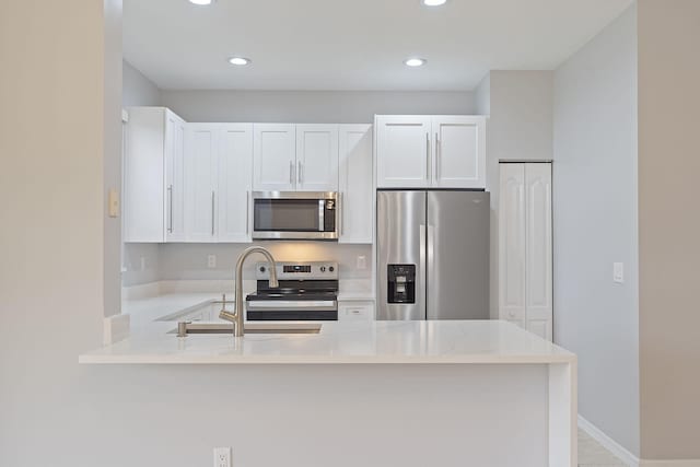 kitchen with kitchen peninsula, white cabinetry, light stone countertops, and stainless steel appliances