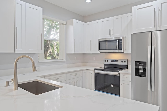 kitchen featuring appliances with stainless steel finishes, white cabinetry, sink, and light stone counters