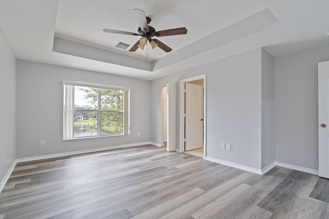 unfurnished room featuring ceiling fan, a textured ceiling, a tray ceiling, and light hardwood / wood-style floors