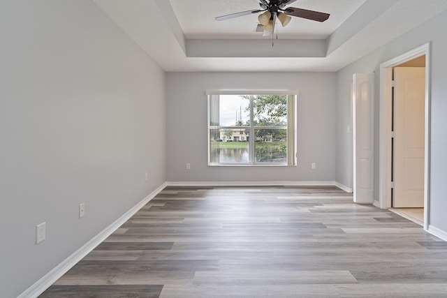 spare room with a textured ceiling, light hardwood / wood-style floors, a tray ceiling, and ceiling fan