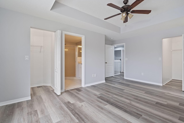 unfurnished bedroom with ceiling fan, light wood-type flooring, ensuite bathroom, and a spacious closet