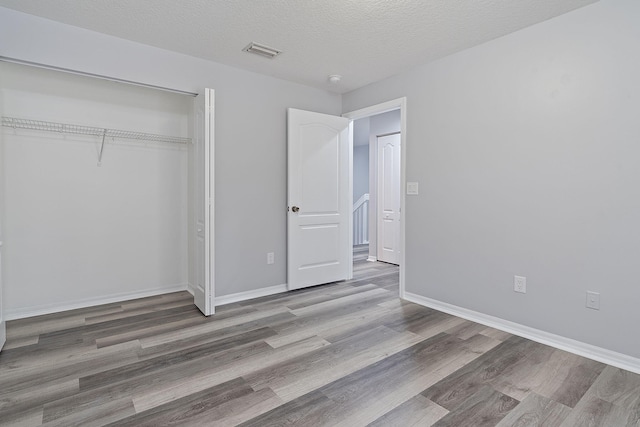 unfurnished bedroom with a textured ceiling, wood-type flooring, and a closet