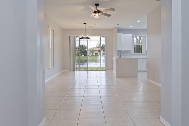 tiled empty room featuring ceiling fan with notable chandelier, a water view, and sink