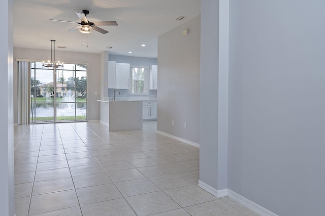 interior space featuring white cabinets, sink, light tile patterned floors, ceiling fan with notable chandelier, and a water view