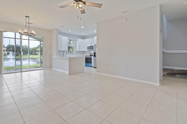 unfurnished living room featuring sink, ceiling fan with notable chandelier, light tile patterned floors, and a water view