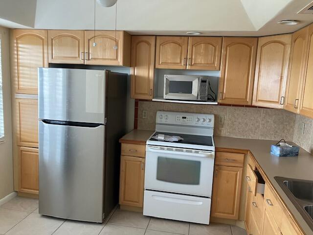 kitchen featuring freestanding refrigerator, electric stove, decorative backsplash, and light brown cabinetry