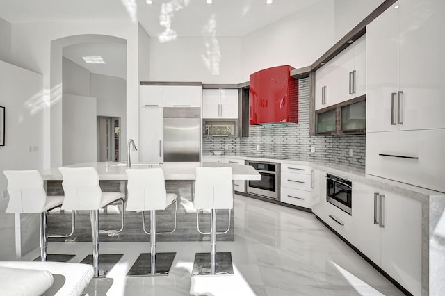 kitchen with built in appliances, decorative backsplash, a kitchen breakfast bar, and white cabinets