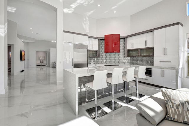 kitchen featuring a kitchen breakfast bar, backsplash, a kitchen island with sink, and white cabinets