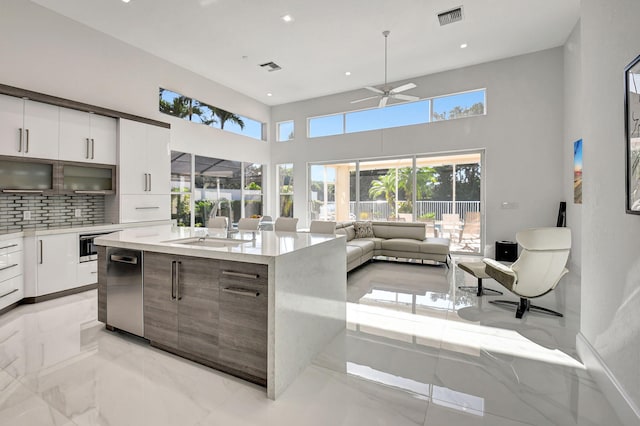 kitchen with ceiling fan, sink, backsplash, an island with sink, and white cabinets