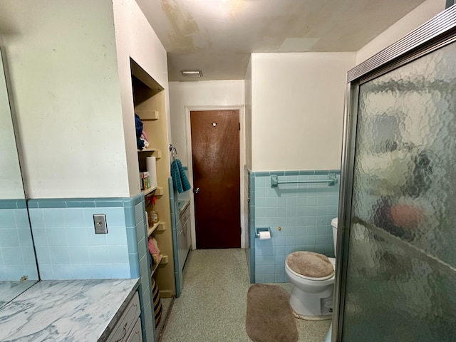 bathroom with vanity, a shower with door, toilet, and tile walls