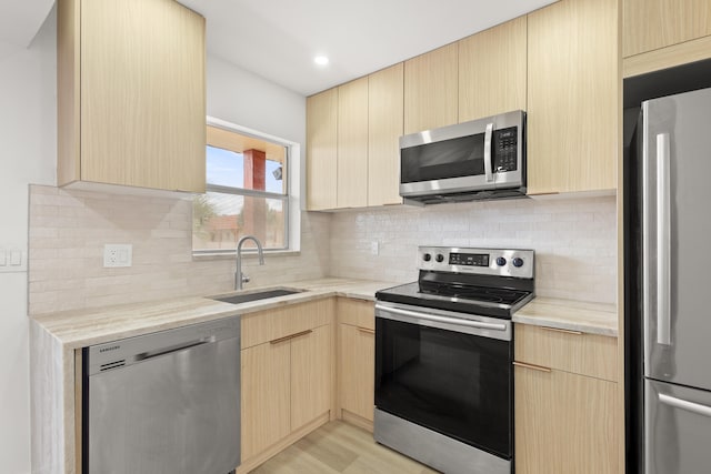 kitchen with backsplash, stainless steel appliances, light wood-type flooring, light brown cabinetry, and sink