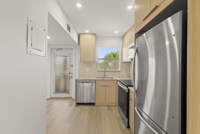 kitchen with light wood-type flooring, tasteful backsplash, sink, stainless steel appliances, and light brown cabinets