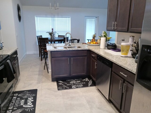 kitchen with stainless steel dishwasher, dark brown cabinetry, a sink, light stone countertops, and a peninsula