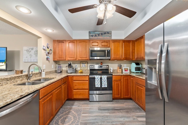 kitchen featuring light stone counters, sink, kitchen peninsula, stainless steel appliances, and light hardwood / wood-style floors