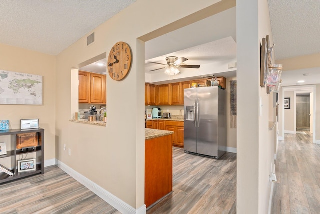 kitchen with light stone counters, a textured ceiling, hardwood / wood-style flooring, stainless steel fridge with ice dispenser, and ceiling fan