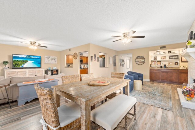 dining room with a textured ceiling, light hardwood / wood-style floors, a fireplace, and ceiling fan