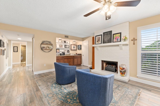 living room featuring a brick fireplace, a textured ceiling, wood-type flooring, ceiling fan, and built in features