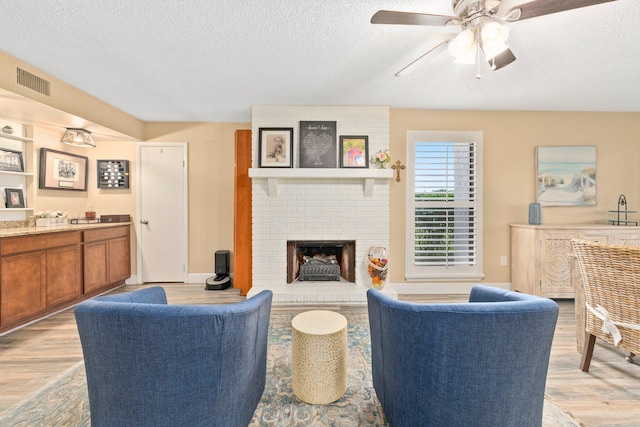 living room featuring light wood-type flooring, a textured ceiling, a fireplace, and ceiling fan