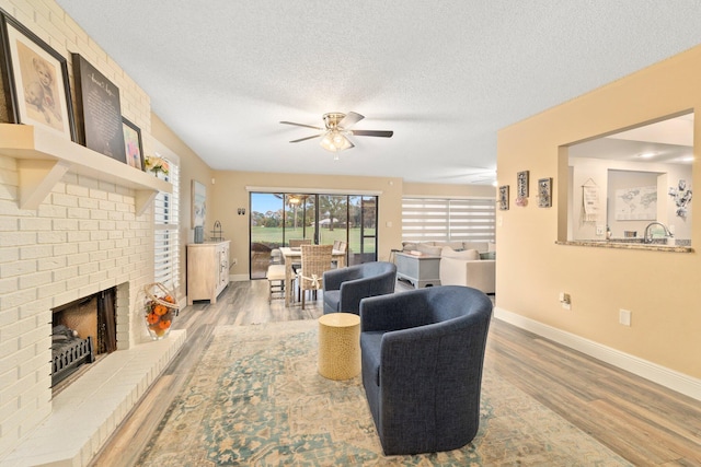 living room with light hardwood / wood-style flooring, a brick fireplace, a textured ceiling, and ceiling fan