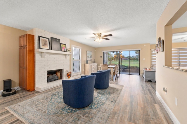 living room with a textured ceiling, wood-type flooring, a fireplace, and ceiling fan