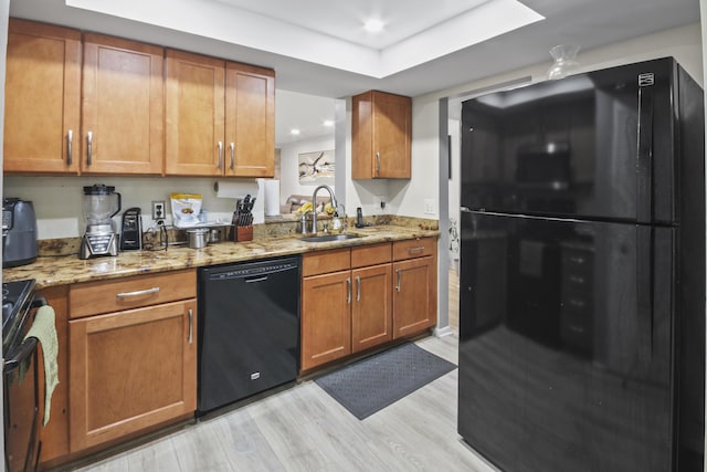 kitchen featuring sink, black appliances, light stone countertops, and light wood-type flooring