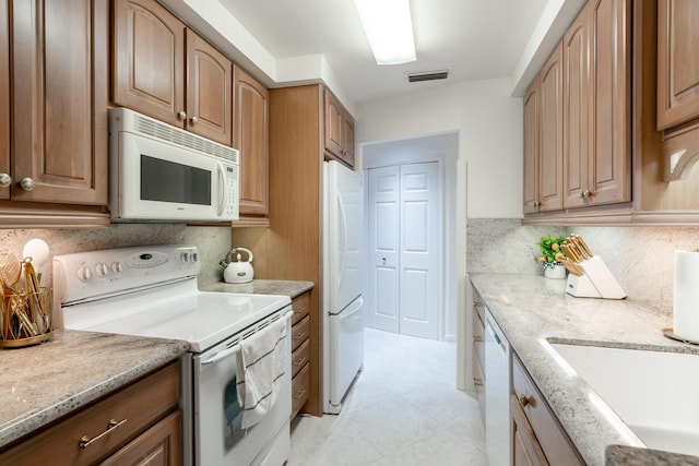 kitchen featuring sink, light stone countertops, white appliances, and backsplash