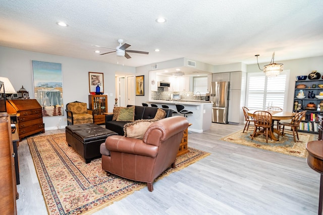 living room featuring ceiling fan, sink, light wood-type flooring, and a textured ceiling