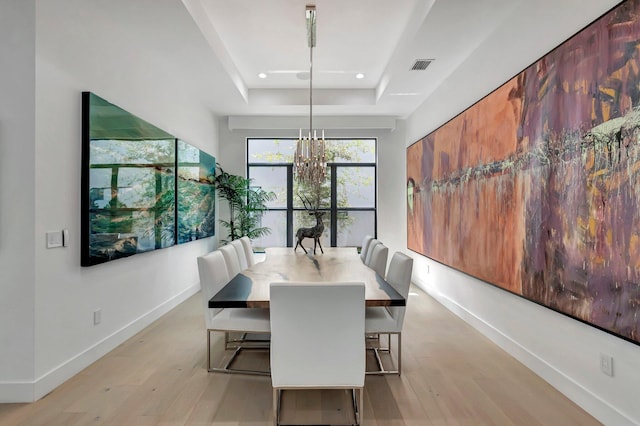 dining space with light hardwood / wood-style floors, a tray ceiling, and a chandelier