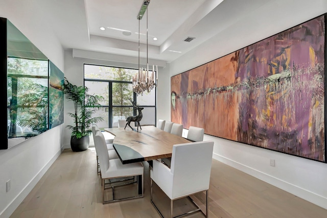 dining space with light hardwood / wood-style floors, an inviting chandelier, and a tray ceiling