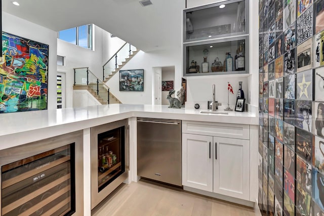 bar featuring light hardwood / wood-style floors, white cabinetry, beverage cooler, and sink