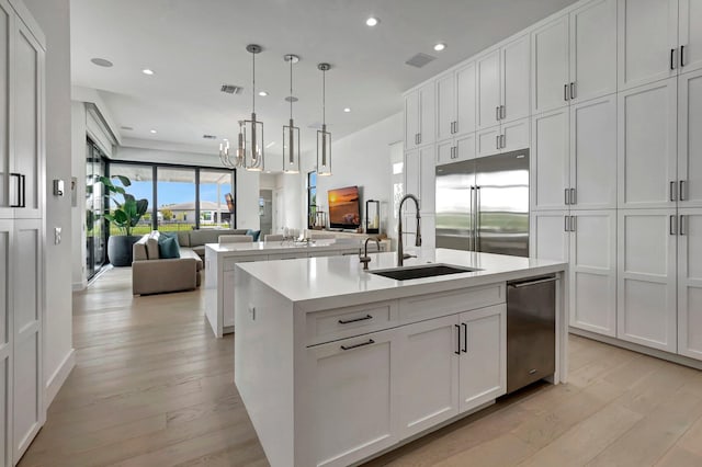 kitchen with light wood-type flooring, stainless steel built in refrigerator, sink, decorative light fixtures, and an island with sink