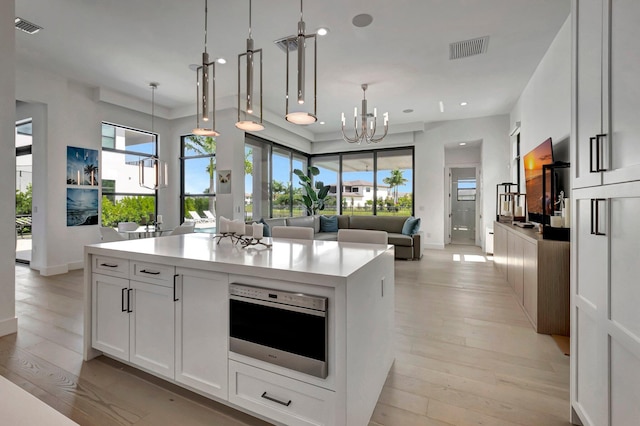 kitchen with light hardwood / wood-style floors, stainless steel oven, white cabinetry, and pendant lighting